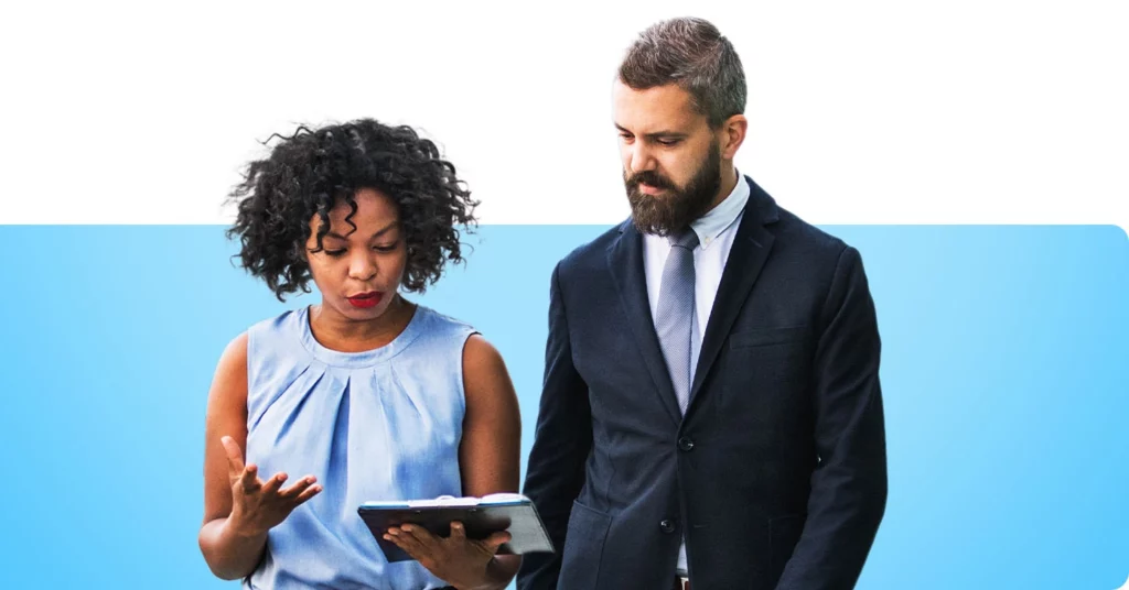 Two busy businesspeople looking at a clipboard to discuss their agenda for the day.